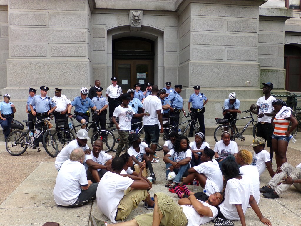 Genser Street residents outside of City Hall on Wednesday afternoon. Patrick Sanyeah, father of the victims, is on the left beneath the man in the gray ball cap. Photo by Kenneth Lipp