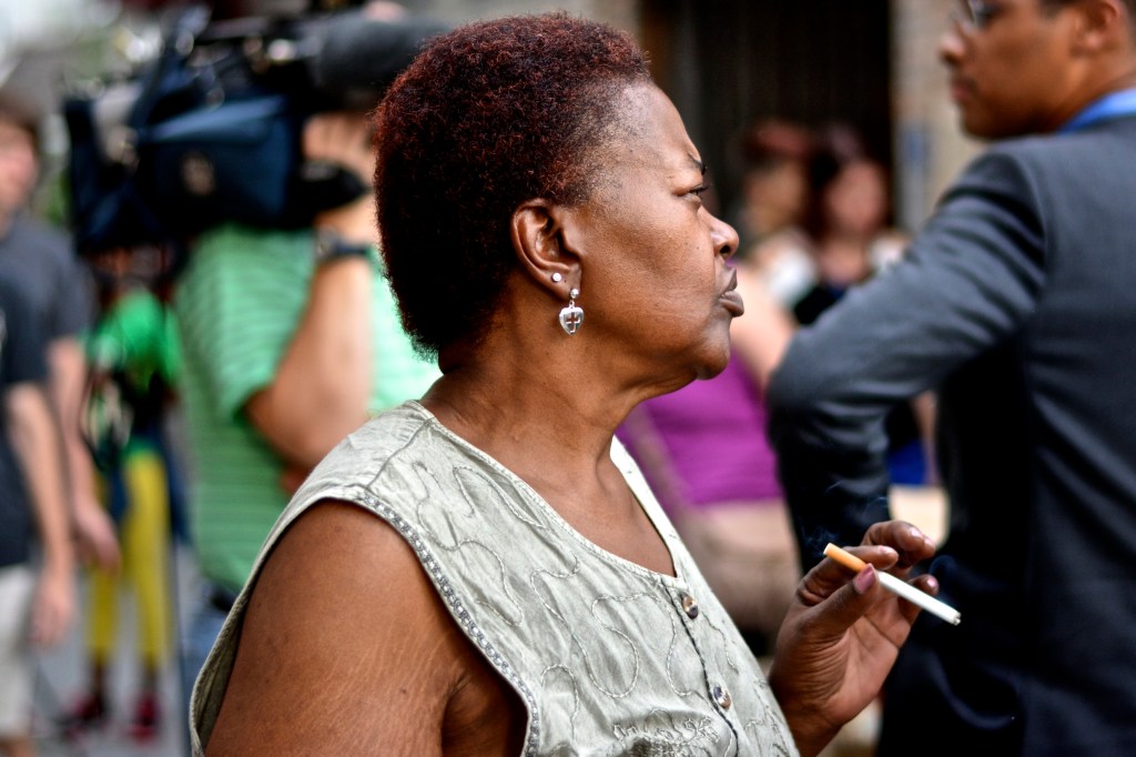 A lady smokes a cigarette while listening to speaker. 