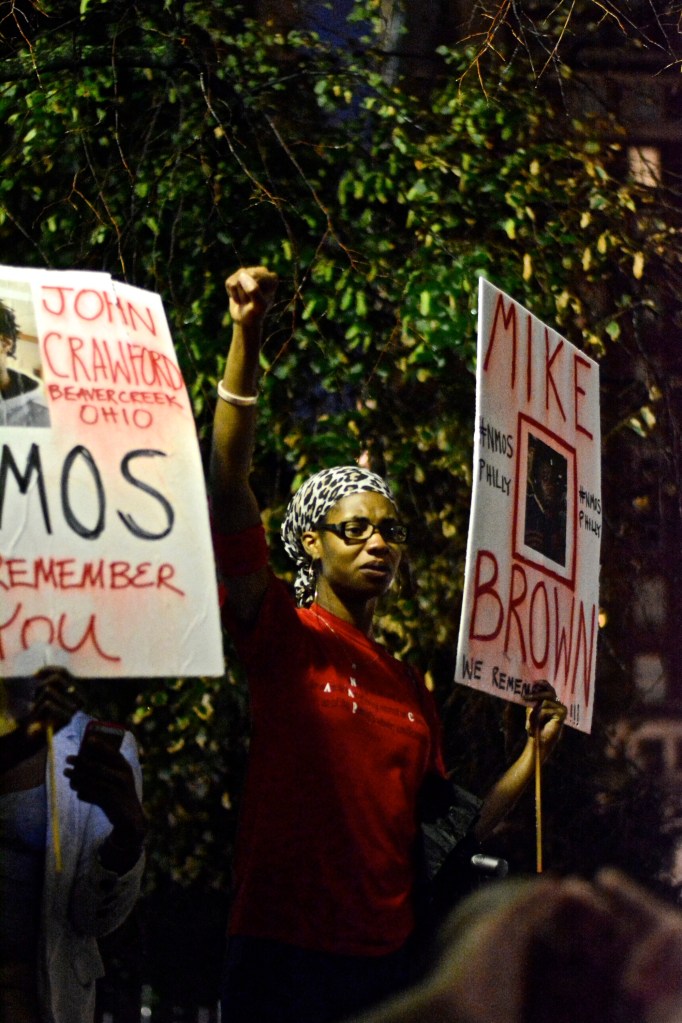 Woman holds fist in the air while leading crowd in chant. ( Photo By Joshua Albert)