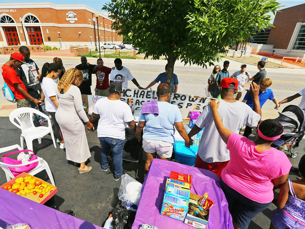 A small group of protesters join hands and bow their heads for a prayer across the street from the police department on Tuesday, Aug. 19, 2014, in Ferguson, Mo. After nine days of unrest following the fatal police shooting of Michael Brown, an unarmed 18-year-old black man, law enforcement and political leaders are looking for ways to restore peace to the community. (AP Photo/Atlanta Journal-Constitution, Curtis Compton) AP