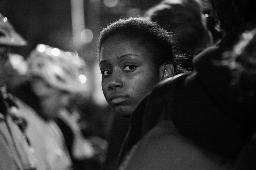 A young woman stands with dozens of protesters outside the 9th District police station Tuesday night.